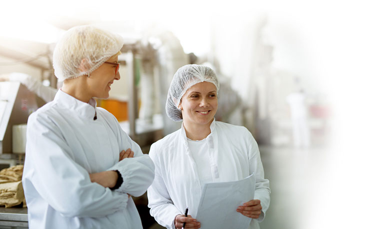 2 femmes collaboratrices portant une blouse et une charlotte discutent dans l'usine de Festi'Fruits